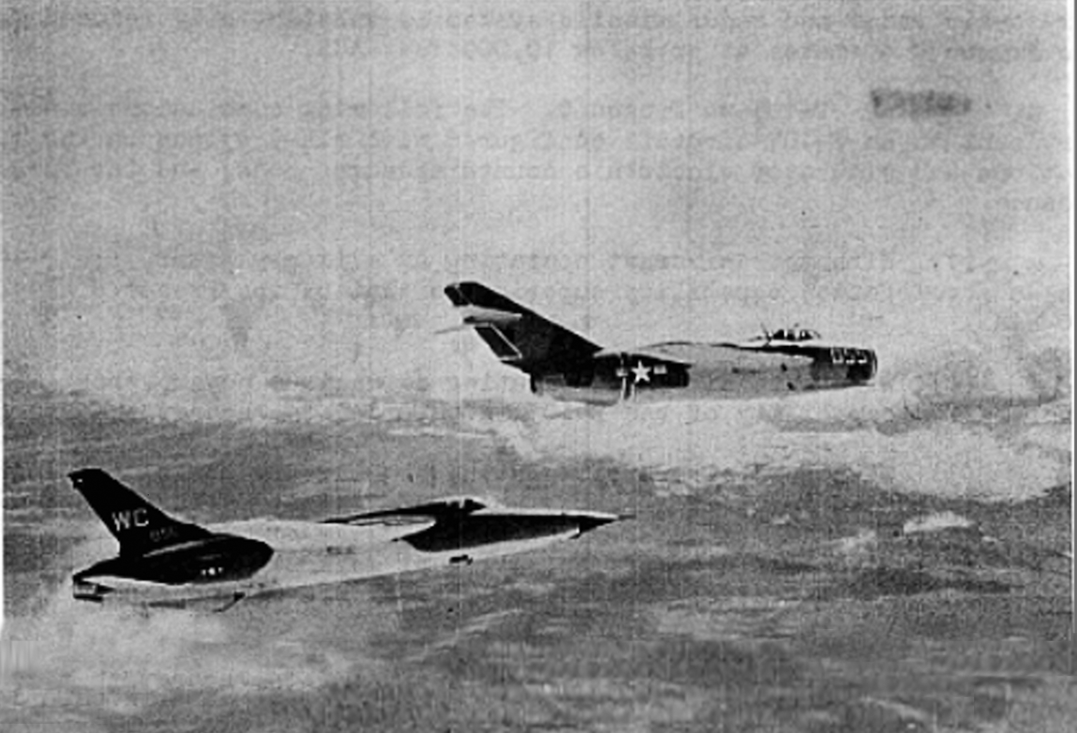 A black-and-white aerial photograph shows a MiG-17, marked with a U.S. insignia, flying alongside a U.S. Air Force F-105 Thunderchief over a layer of clouds.